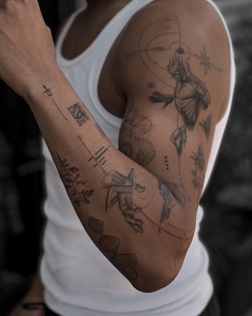 Man's arm and shoulder with a collection of black ink artistic tattoos.