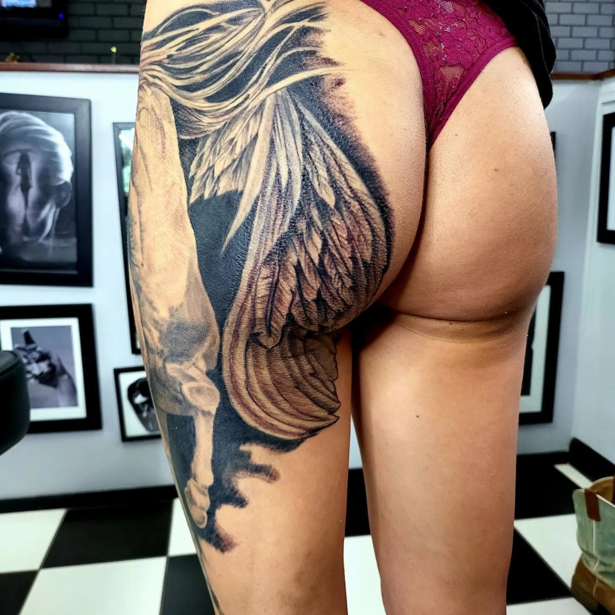 Large black and grey winged figure tattoo on a woman's upper thigh and hip