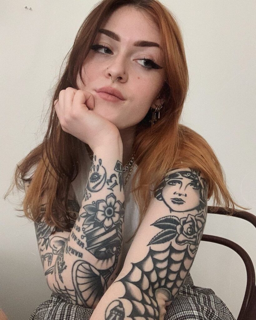 Woman with reddish-brown hair showing full traditional tattoo sleeves on both arms.