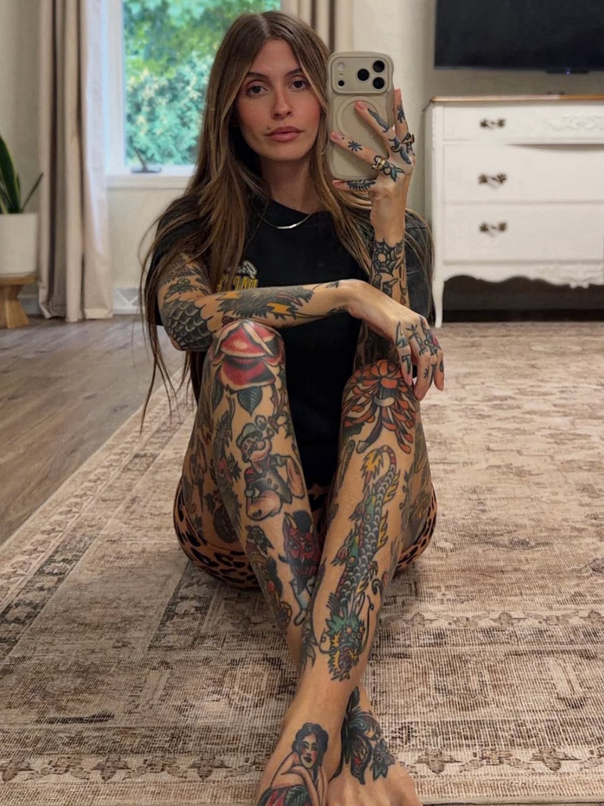 Woman with extensive traditional tattoos on her arms and legs taking a mirror selfie.