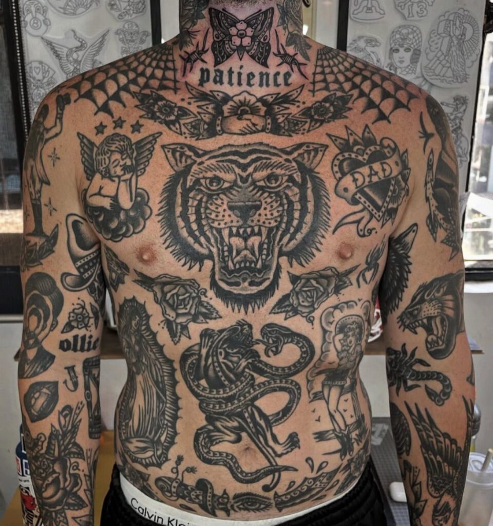 Man's chest and arms covered in bold black ink traditional style tattoos.
