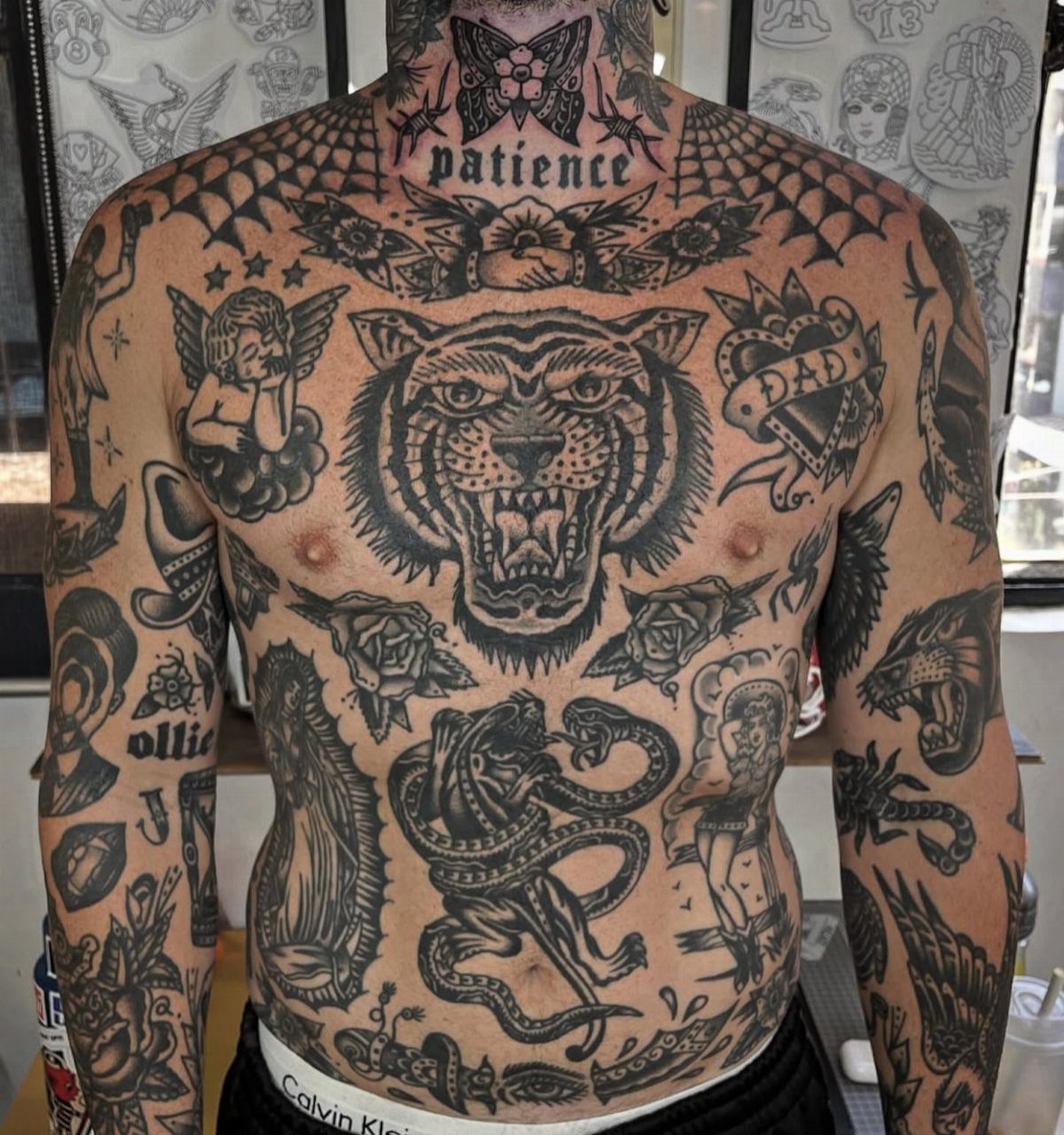 Man's chest and arms covered in bold black ink traditional style tattoos.