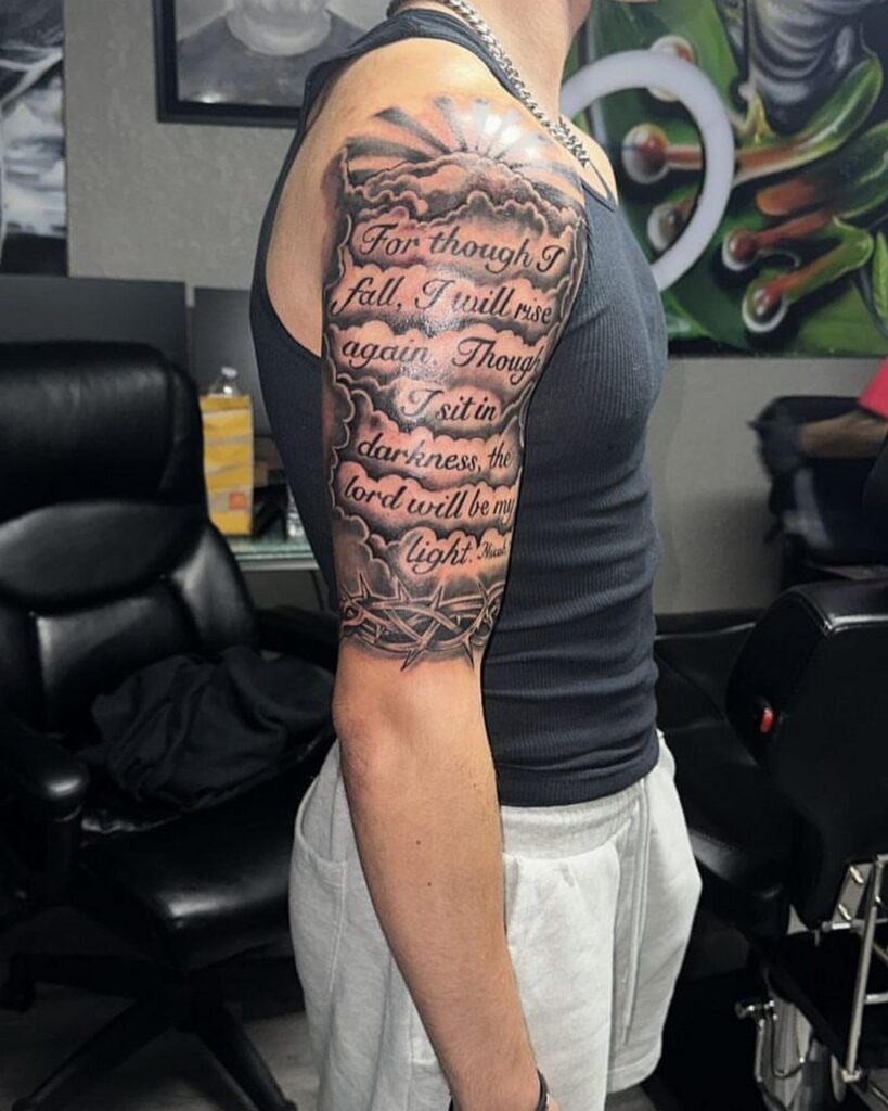 Upper arm tattoo with religious script, clouds, and light rays on a man.