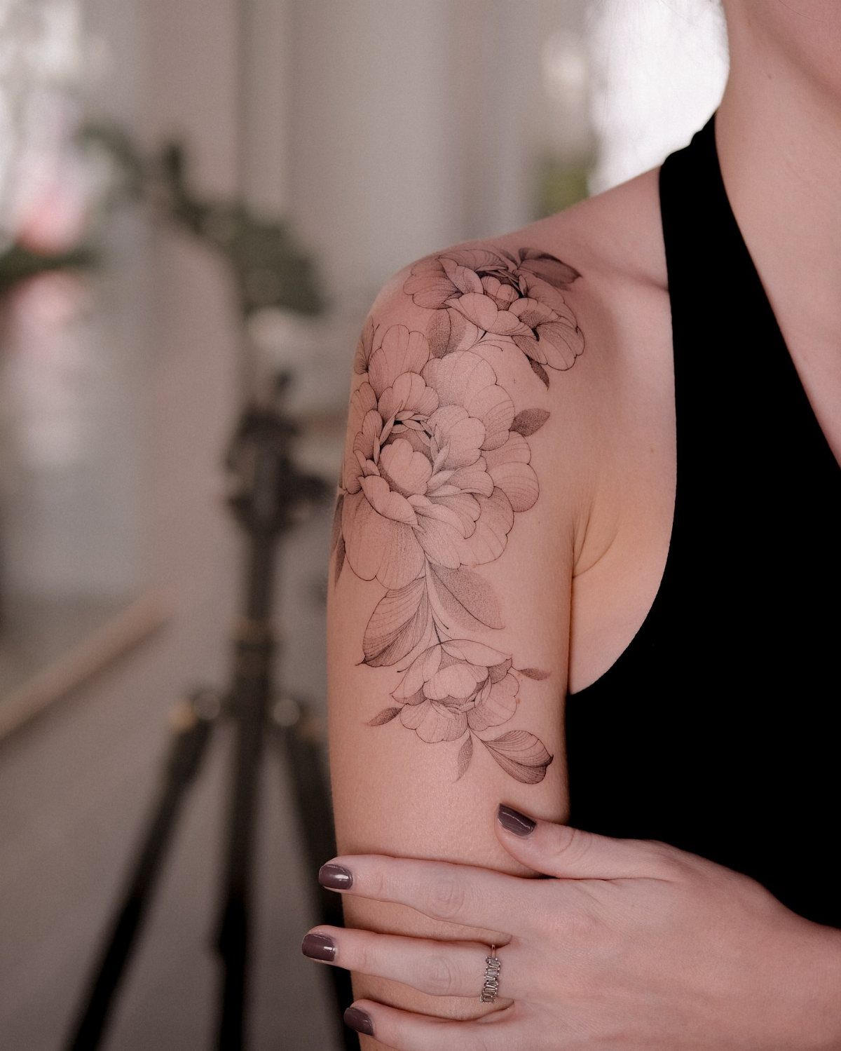 Woman's upper arm with a detailed black ink floral peony tattoo.