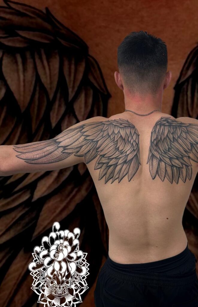 Man's back with large detailed black and grey wing tattoos on shoulder blades