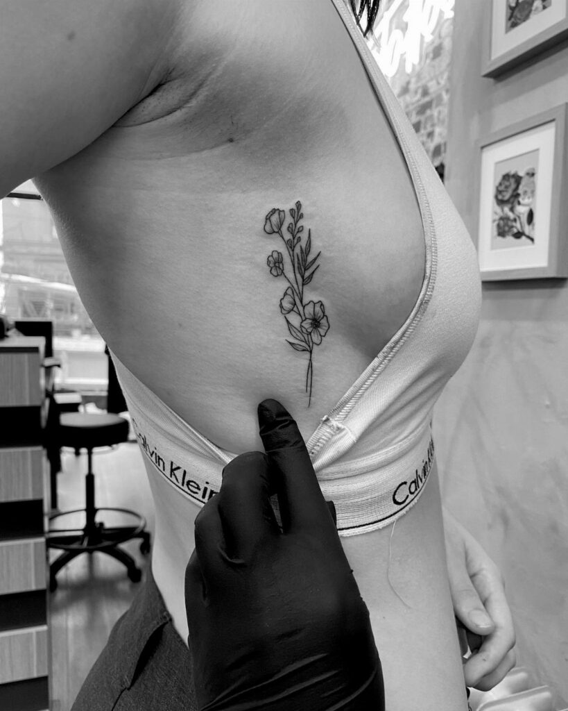 Woman's side torso featuring a delicate floral line-art tattoo on the ribcage.
