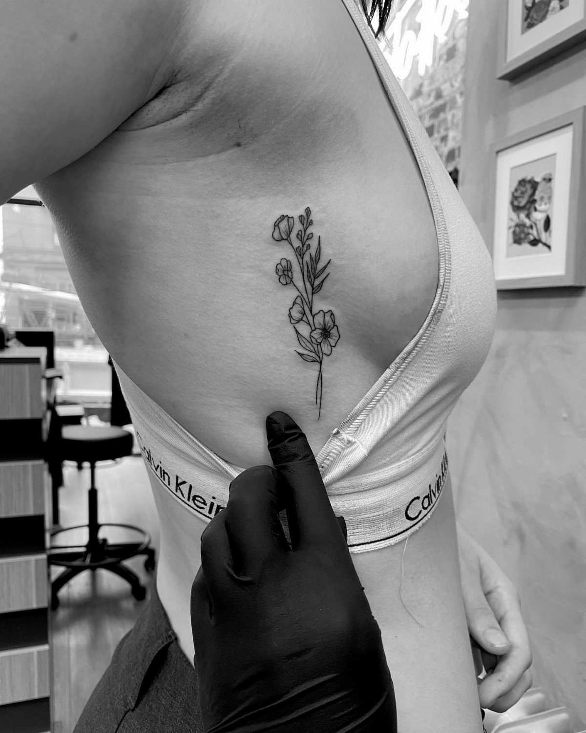 Woman's side torso featuring a delicate floral line-art tattoo on the ribcage.