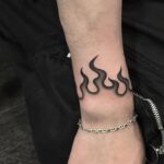 Wrist with a black flame tattoo, silver chain bracelet, and a silver ring.