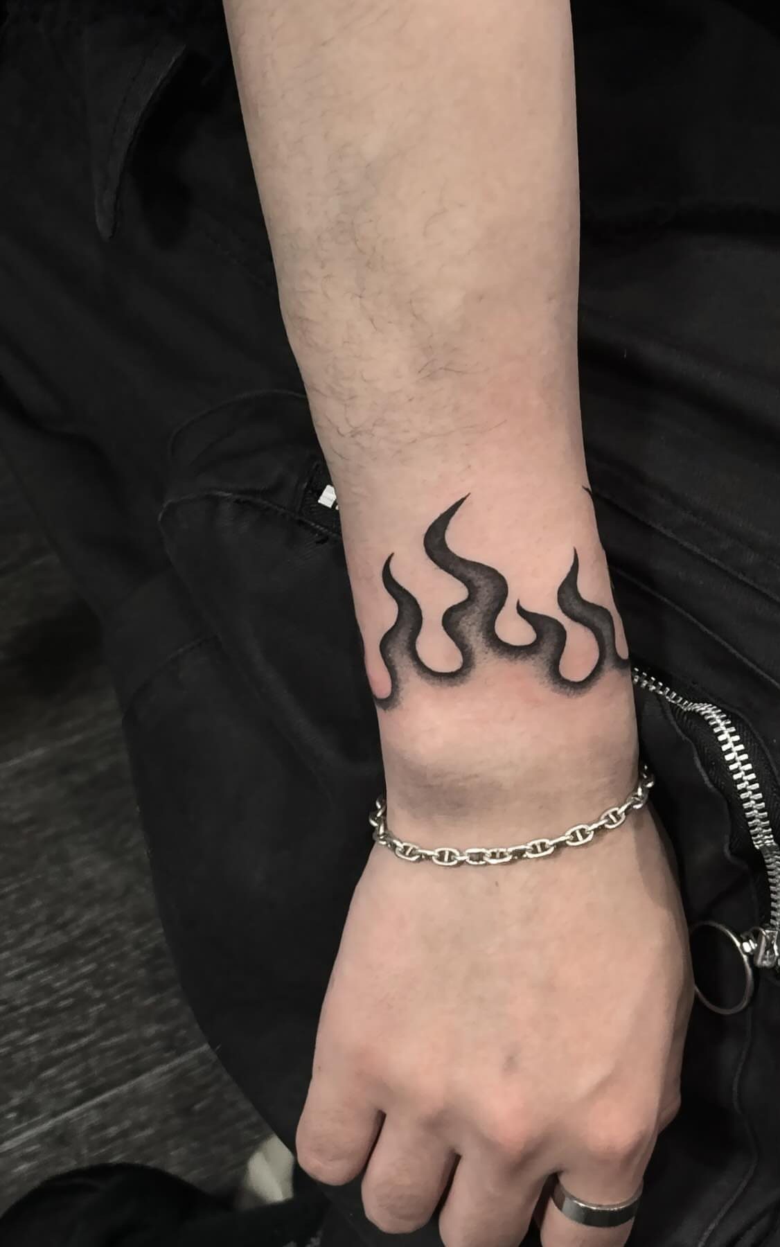 Wrist with a black flame tattoo, silver chain bracelet, and a silver ring.